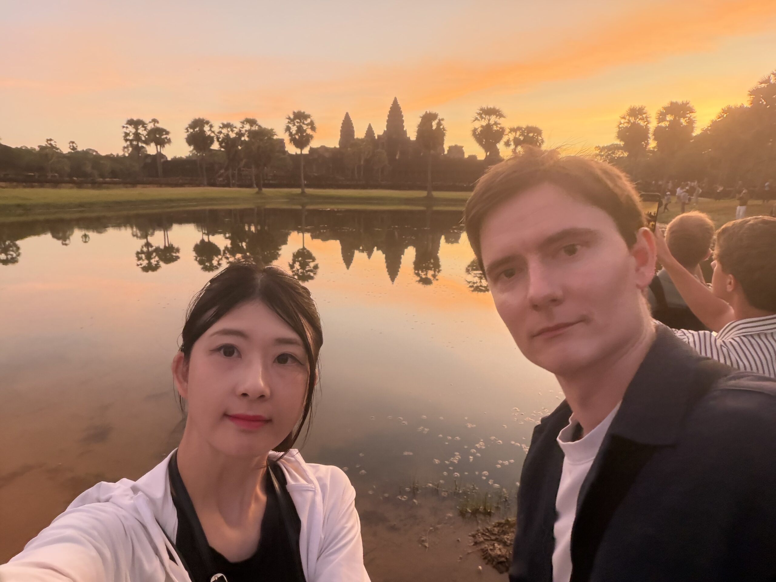 Two people smiling by a lake at sunset